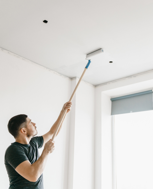 Ein Maler streicht mit weißer Farbe einen Deckenabschnitt in einer leeren Wohnung